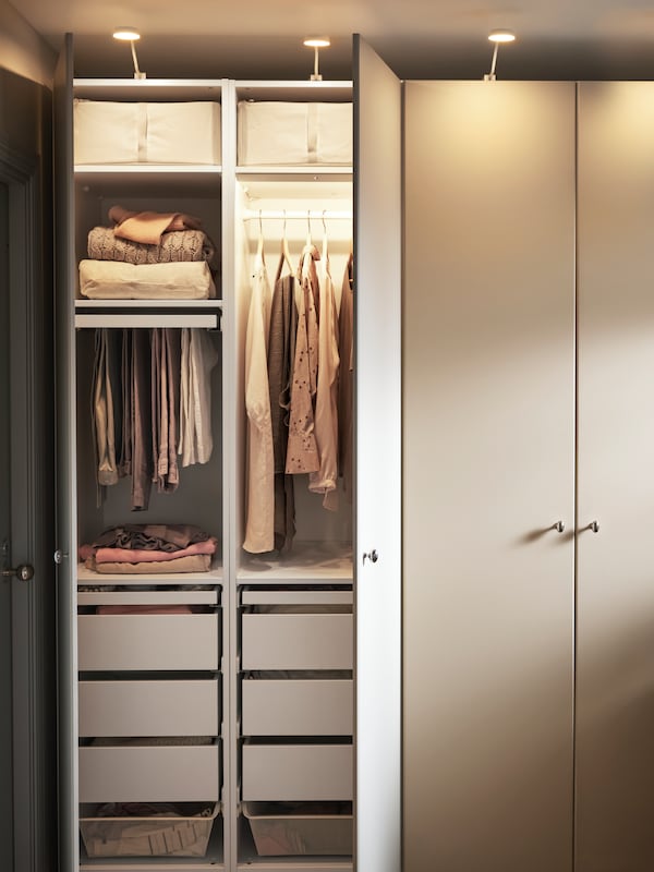 A PAX/REINSVOLL wardrobe combination with two doors open, with hanging clothes, shelves, baskets and drawers inside.