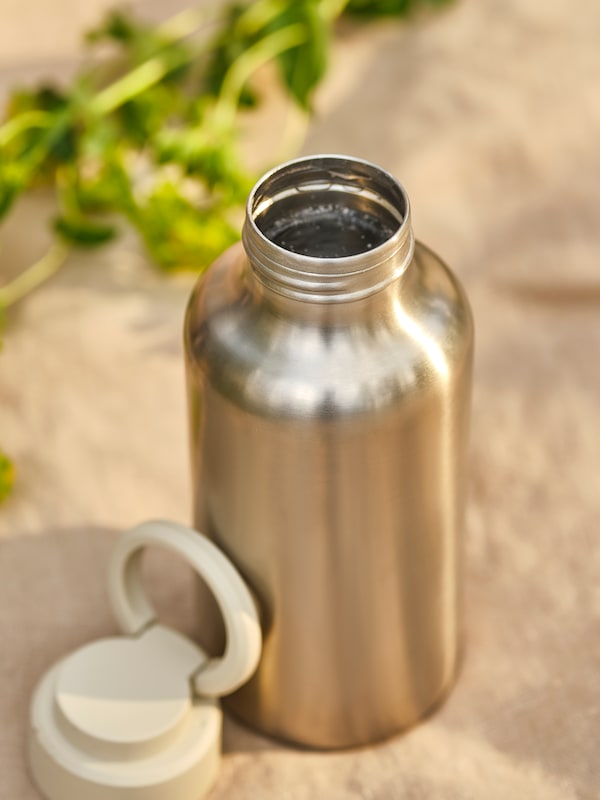 An ENKELSPÅRIG stainless steel water bottle, its beige cap off, placed on a rough, sunlit surface.