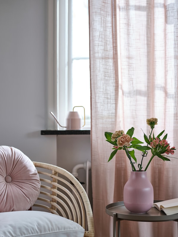 A pink GRADVIS vase on a GLADOM tray table beside a rattan armchair by a window with light-pink SILVERLÖNN sheer curtains.
