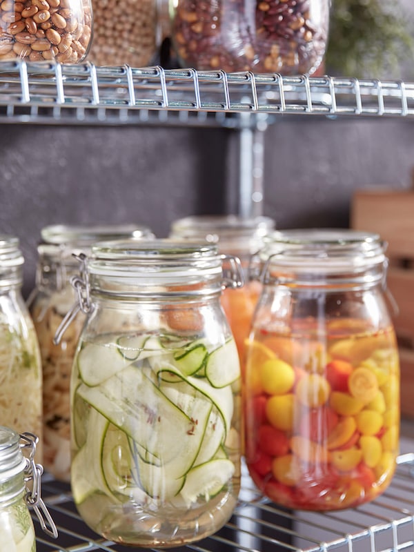 Pickled vegetables in pickling jars on metal wire kitchen shelving. 