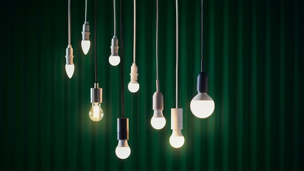 Several SOLHETTA bulbs of different sizes and shapes are hanging from the ceiling in front of a dark green background.