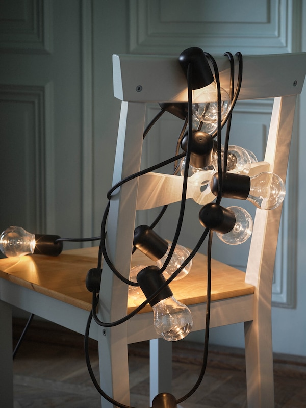 Sleek metal & glass string lights tangled on white & beige farmhouse style kitchen chair. 