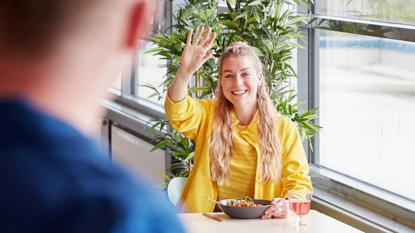 Smiling IKEA co-worker inviting a colleague to join her for lunch in the canteen.