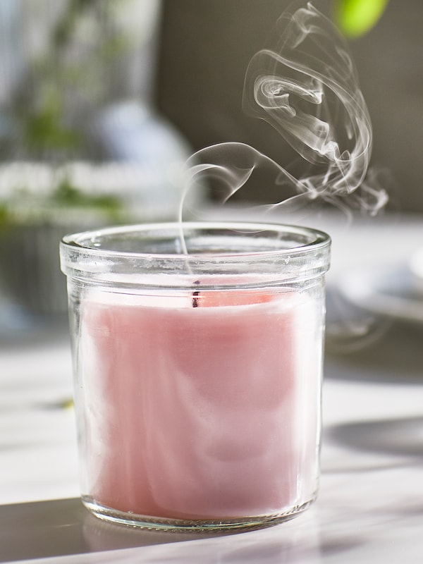 Smoke rises from the wick of a pink LUGNARE scented candle in glass which has just been put out.