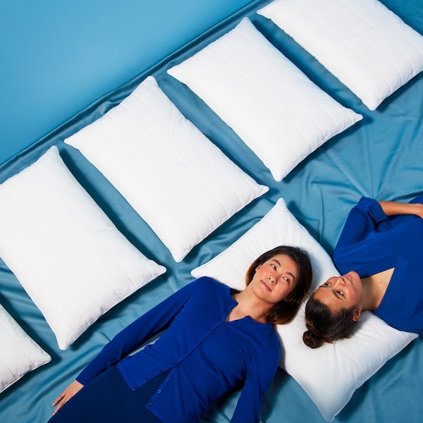 Two people have their heads on the same pillow but are lying in opposite directions. Beside them are some other pillows.