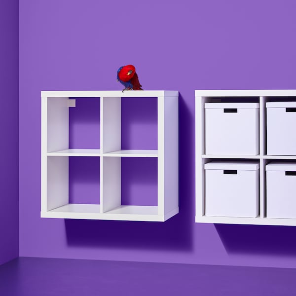 Two white KALLAX shelving units hang against a purple wall, one empty, and the other with white storage boxes on the shelves.