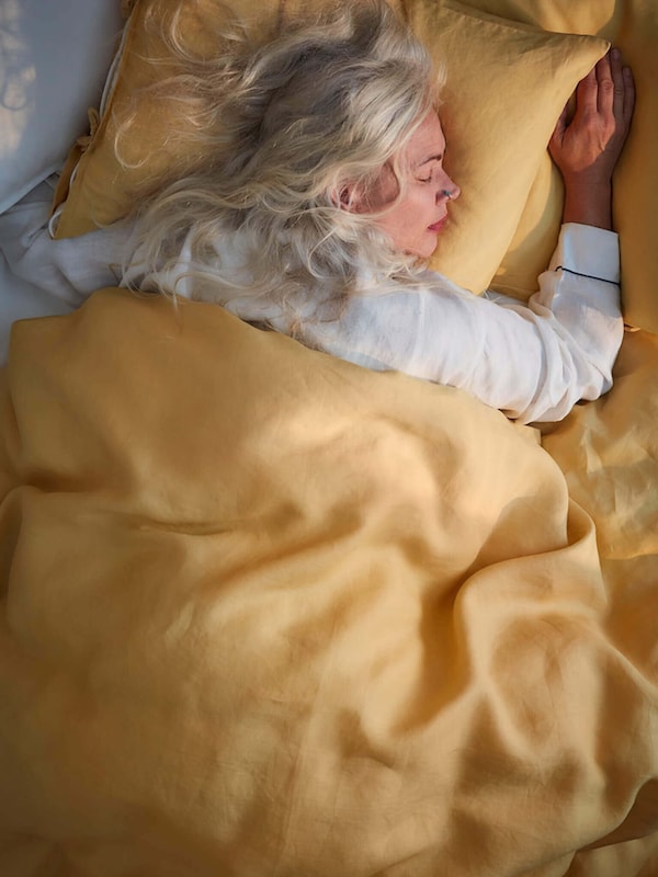Woman in pajamas sleeping on a yellow pillow and covered by yellow blanket. 