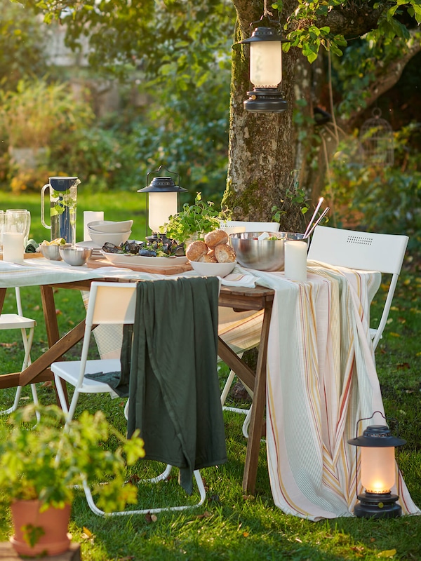 Wood table outdoors with white folding chairs draped with cloth