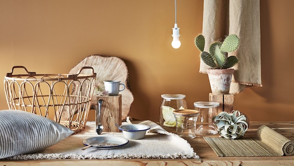 Wooden dining room table with bamboo mat, glass jars, plants and plateware. 